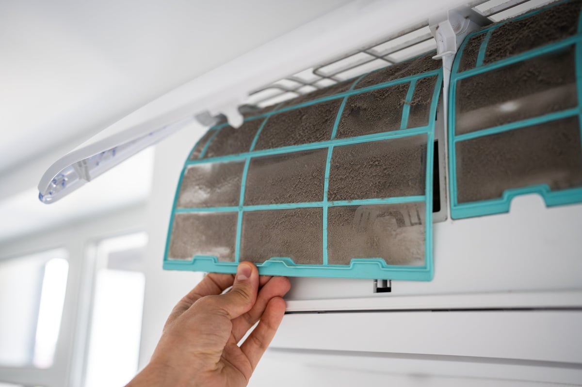 Person removing dirty dusty air conditioner filter for washing and cleaning