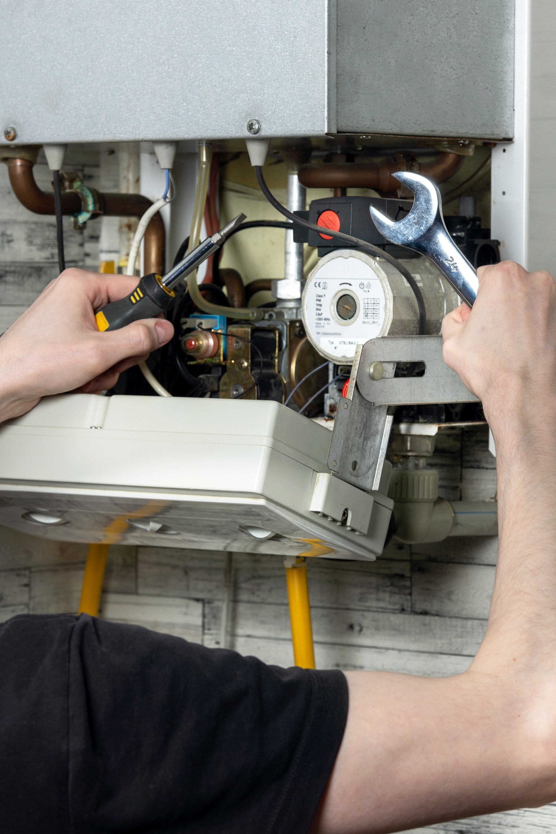 Maintenance of an electric water heating boiler; a man with a wrench and a spanner in his hands is repairing the boiler