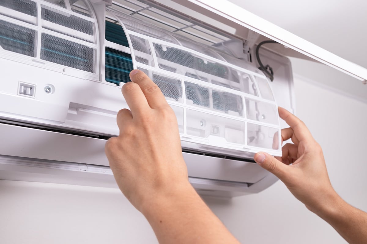 Close up of man inserting new filter into air conditioner unit during regular maintenance