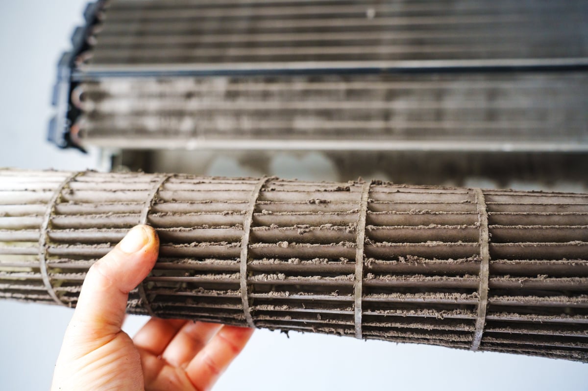 A person holds a dirty air conditioner filter showing dust buildup