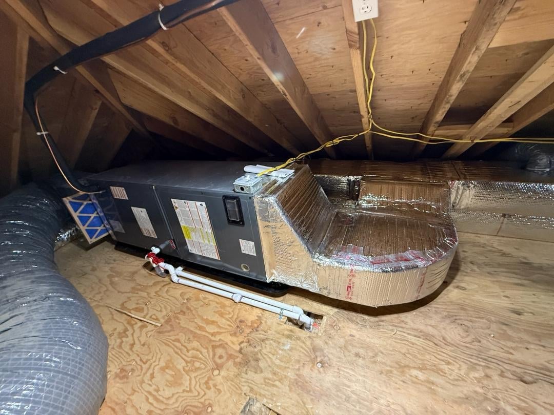 HVAC unit with silver ductwork installed in crawl space under wooden ceiling joists