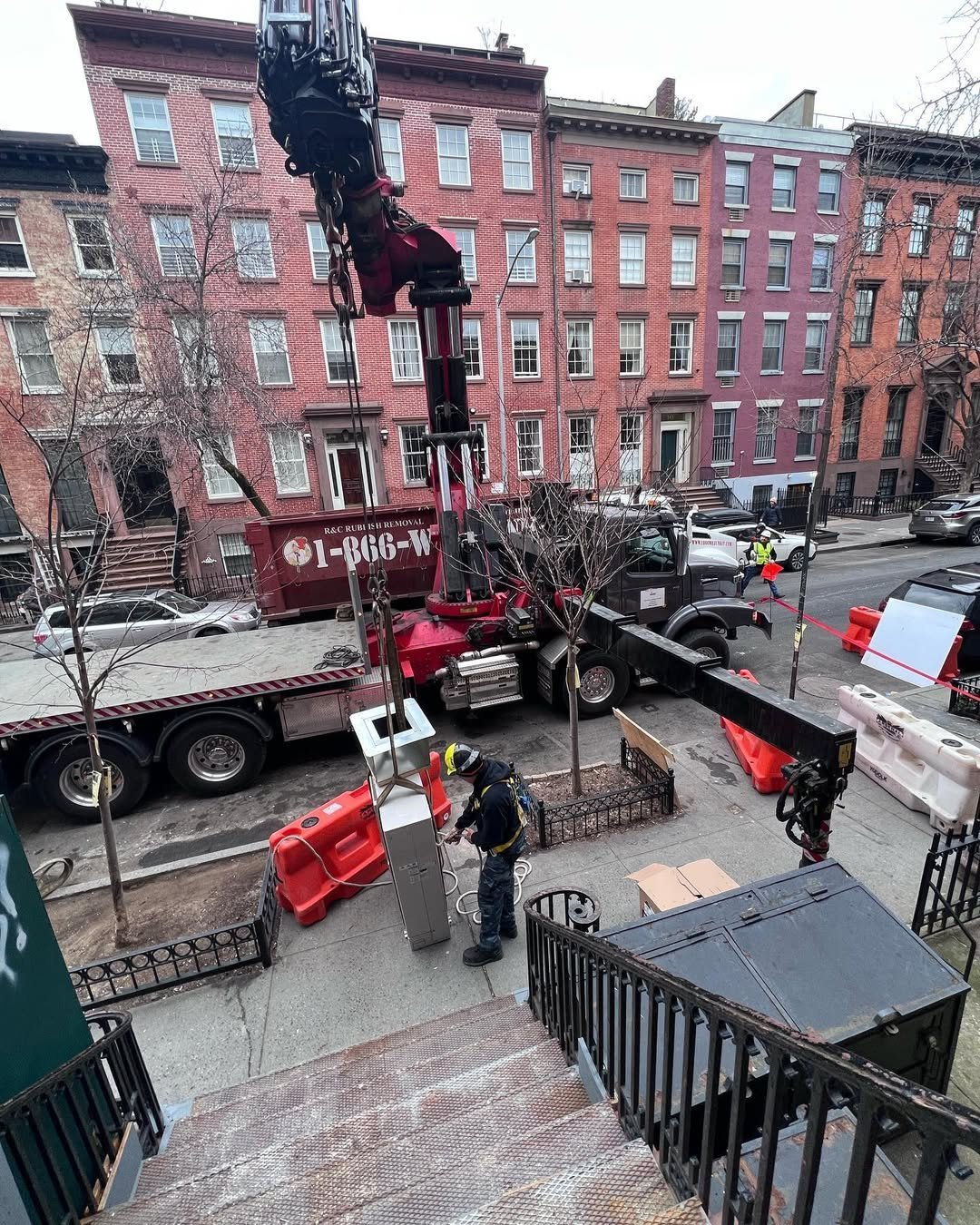 Red construction crane truck on city street with historic brick buildings in background and workers nearby