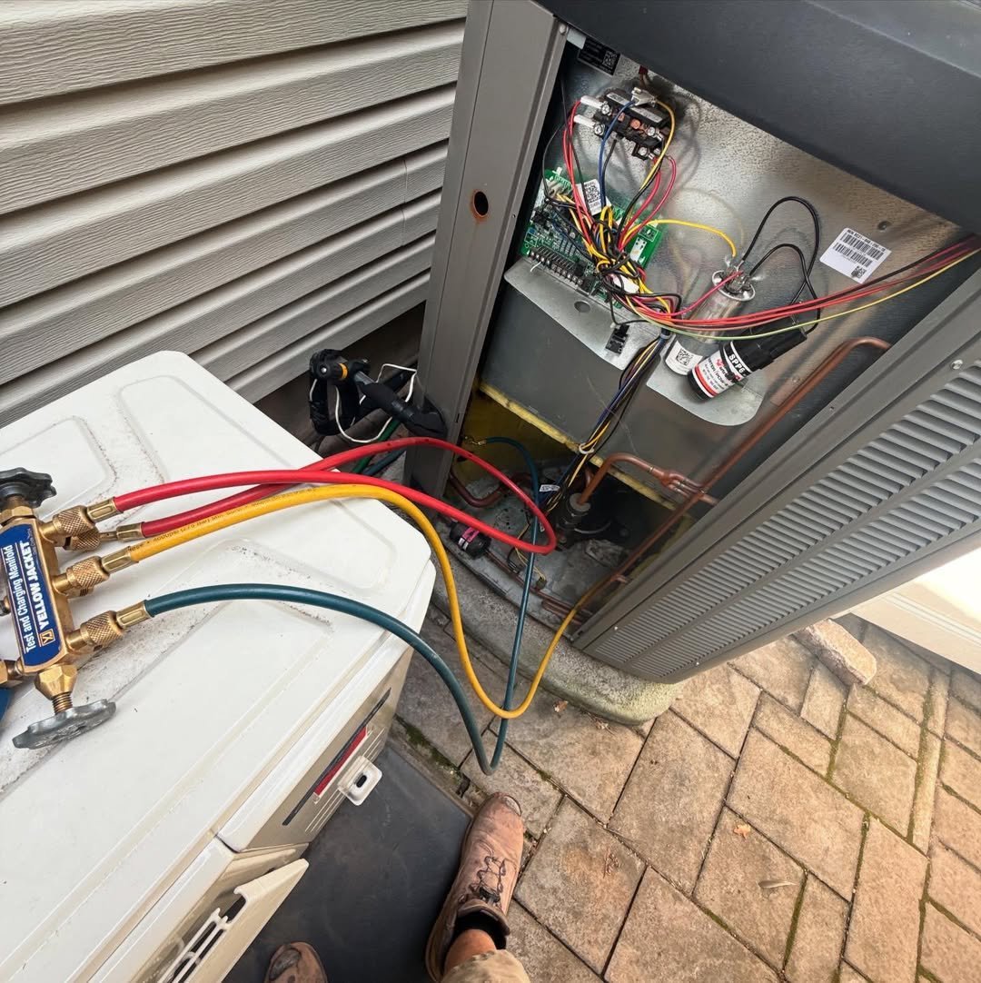 Open HVAC unit showing internal electrical components, circuit board, and colored wiring with technicians hands visible during service work.