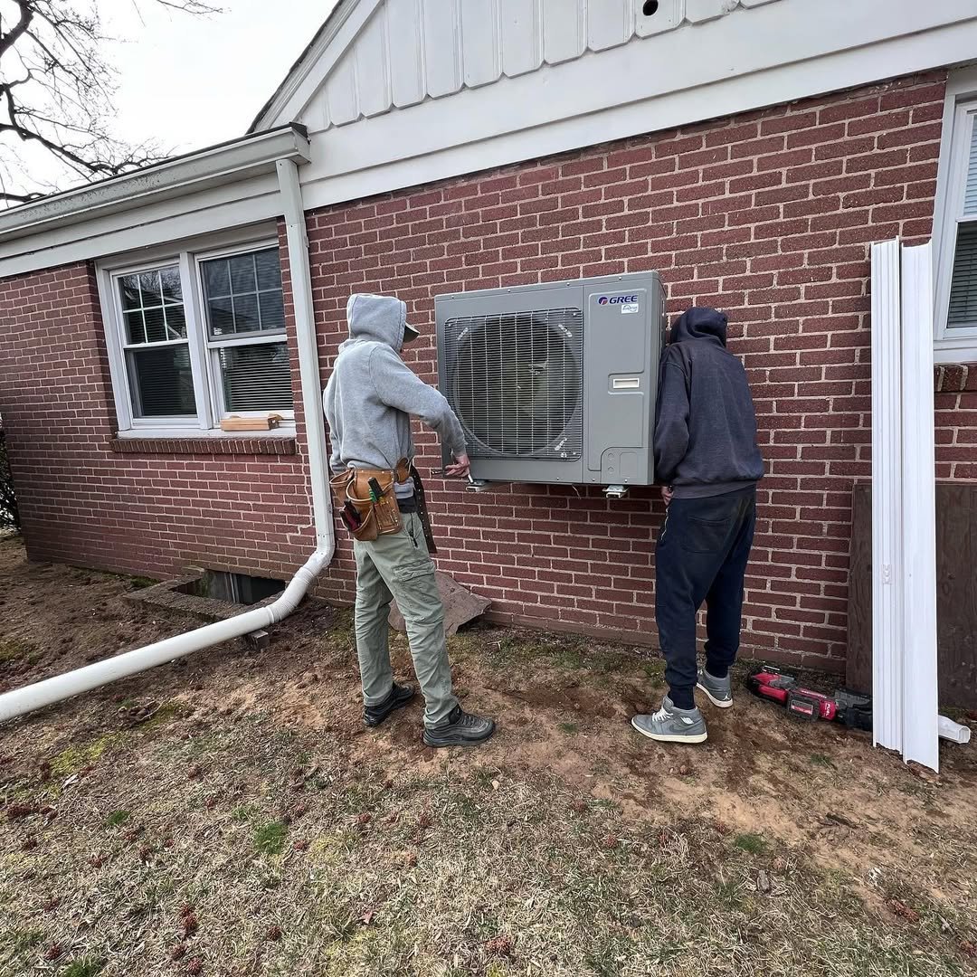Two technicians installing an outdoor air conditioning unit on the brick exterior of a residential home