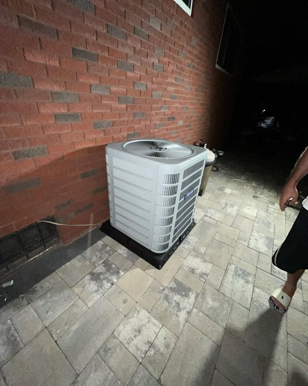 White HVAC air conditioning unit installed against red brick wall on concrete patio