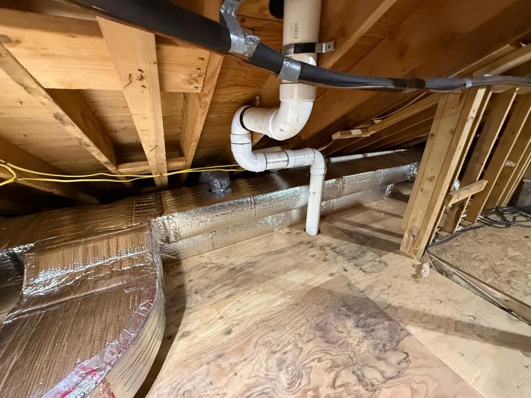 Basement space under wooden joists showing white HVAC ducts and various building materials