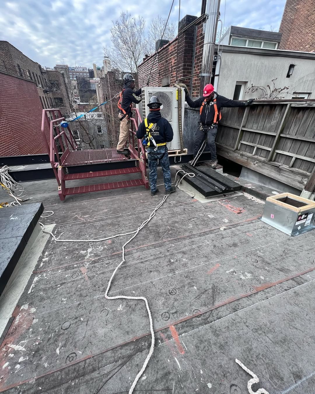 Workers in safety gear on a city rooftop performing construction or maintenance work with ropes and equipment